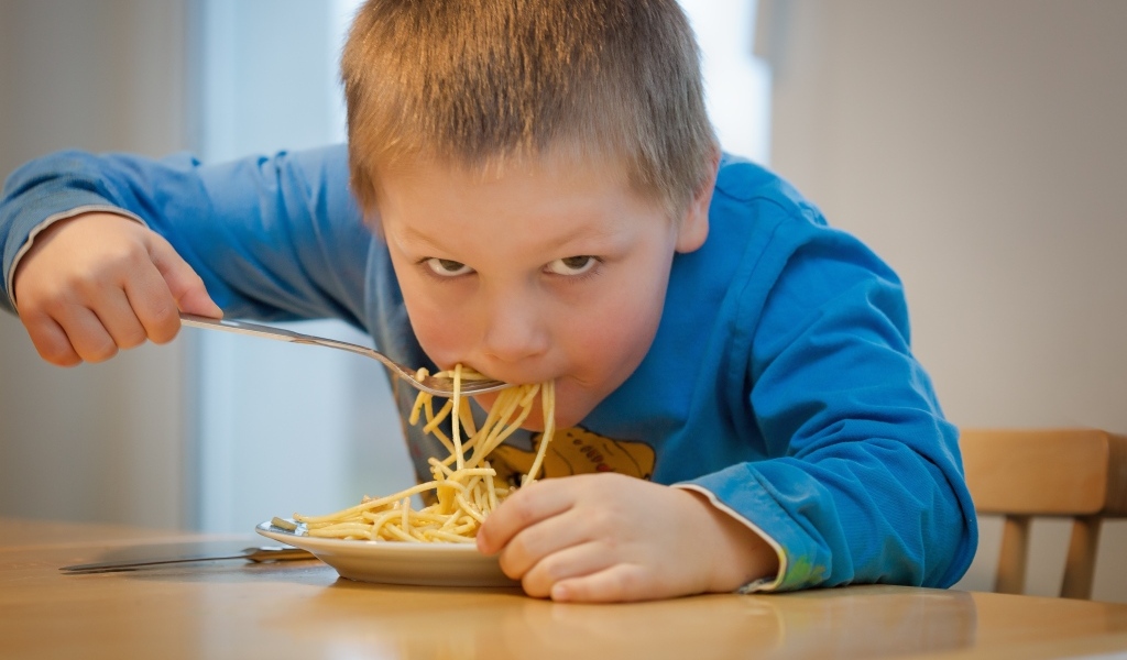 Маленький мальчик ест макароны