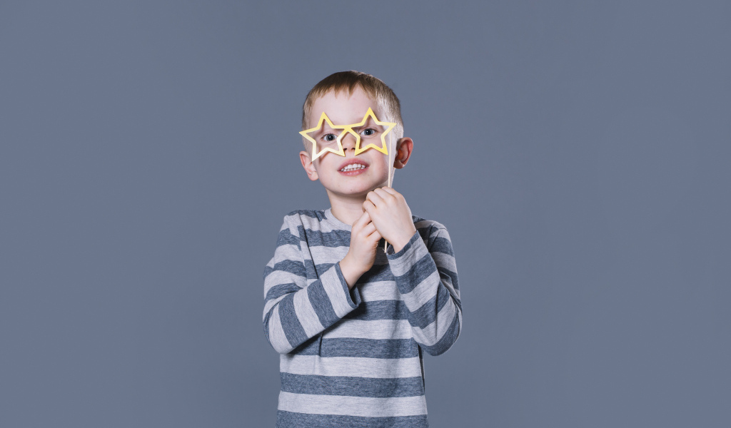 Маленький мальчик с очками в форме звезд на сером фоне