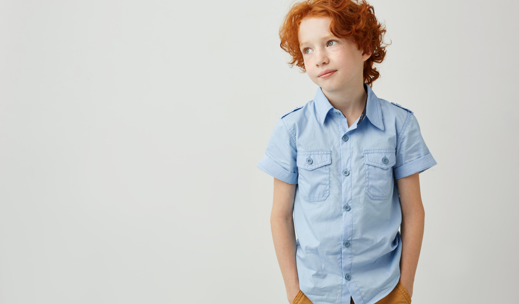 Рыжеволосый мальчик на фоне серой стены