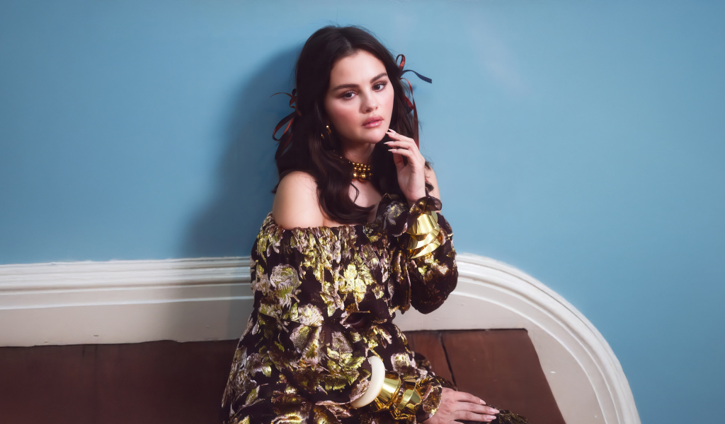 Актриса Селена Гомес на диване на фоне серой стены