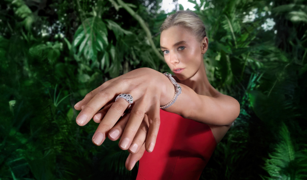 Актриса Ванесса Кирби в красном платье с кольцом на руке на фоне зарослей