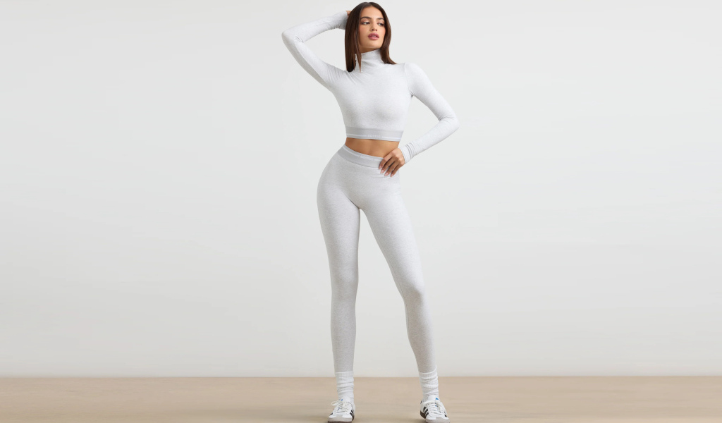 Стройная спортивная девушка в костюме позирует на сером фоне