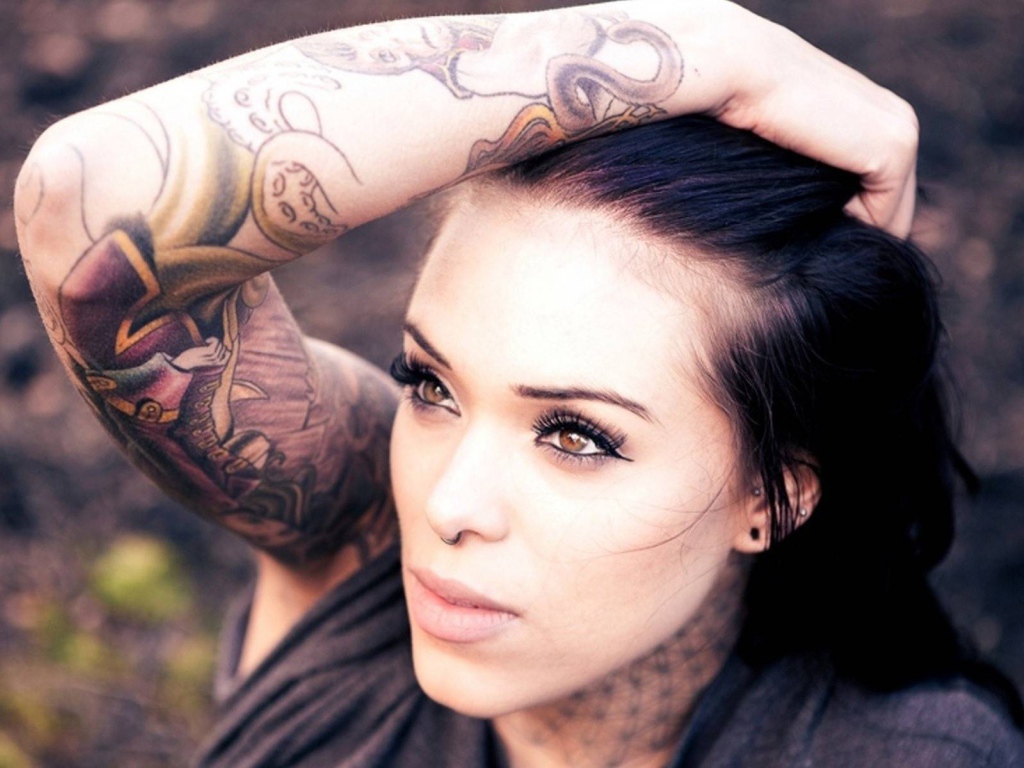 Девушка брюнетка с пирсингом в носу и татуировкой на руке