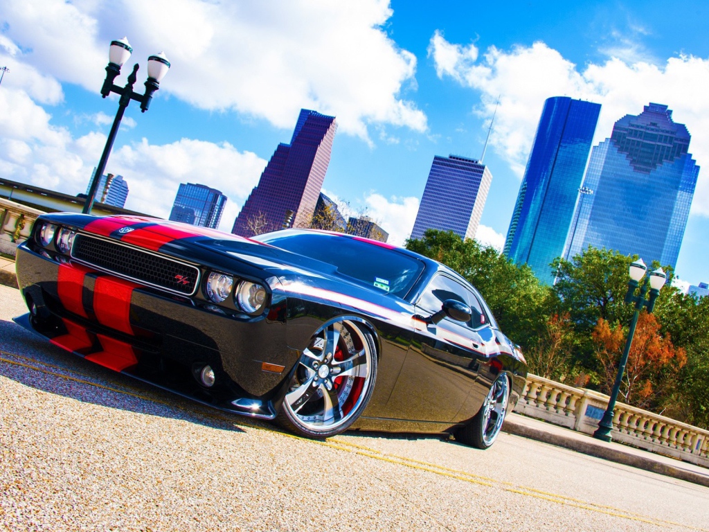 Черный Dodge Challenger с красными полосами на фоне небоскребов