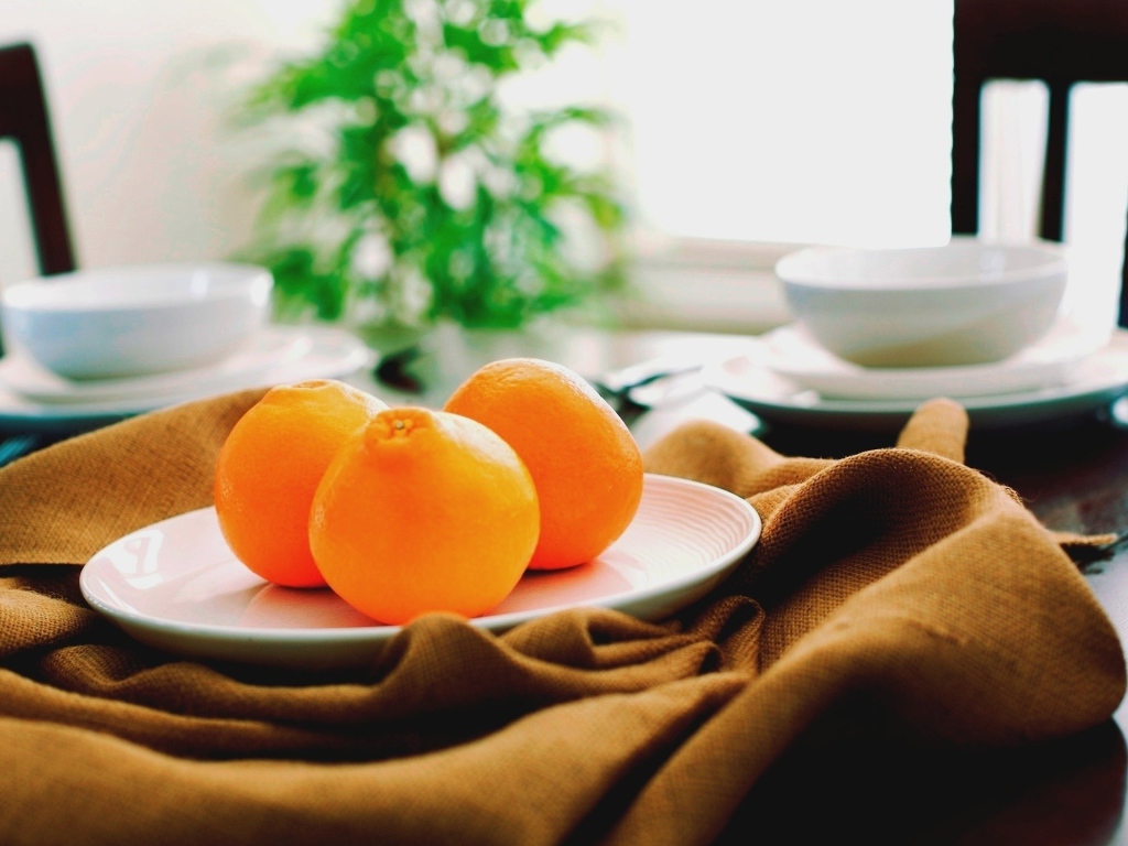 Три апельсина на белой тарелке