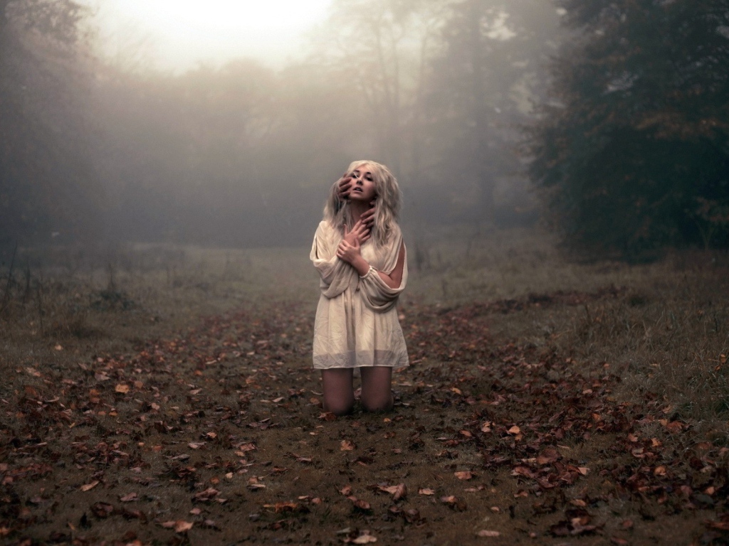 Блондинка в белом платье стоит на коленях среди леса