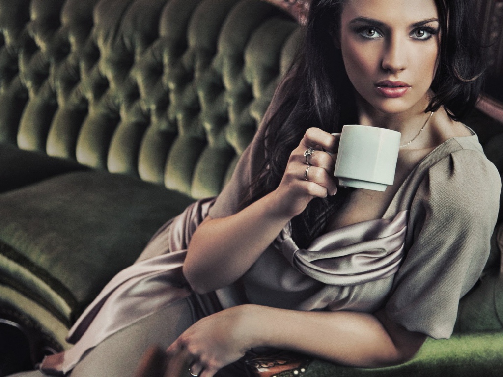 Брюнетка с чашкой кофе сидит на диване
