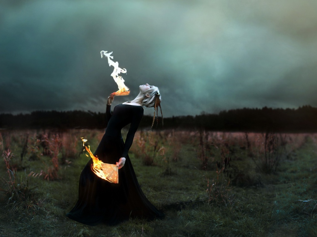 Девушка в черном платье играет с огнем