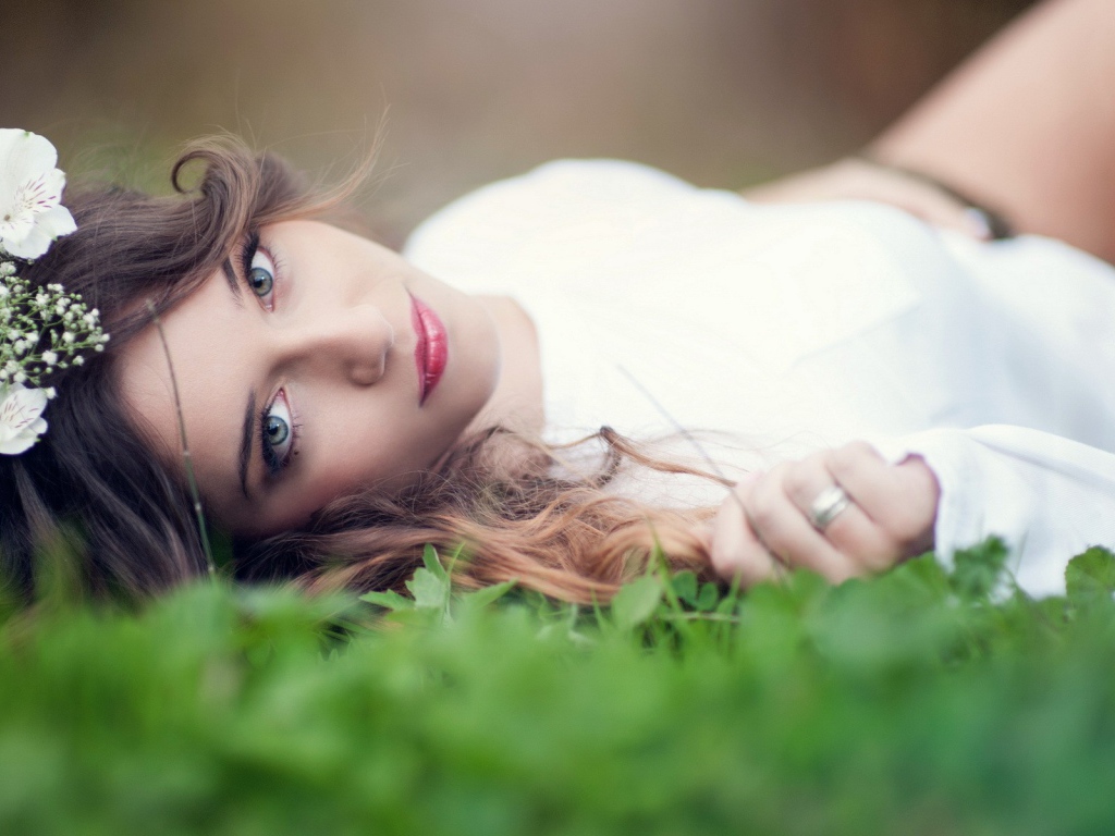 Девушка в белом платье с украшением в волосах лежит на траве