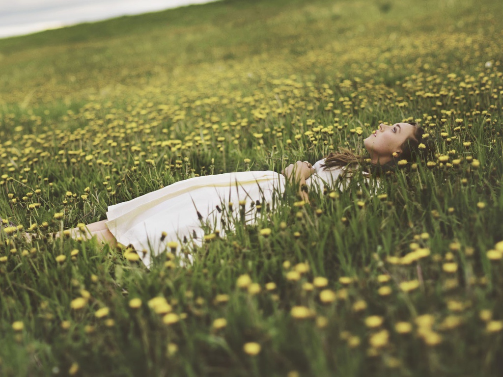 Девушка лежит в поле среди одуванчиков