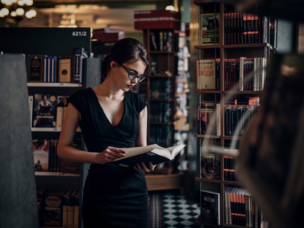 Девушка читает среди книжных полок