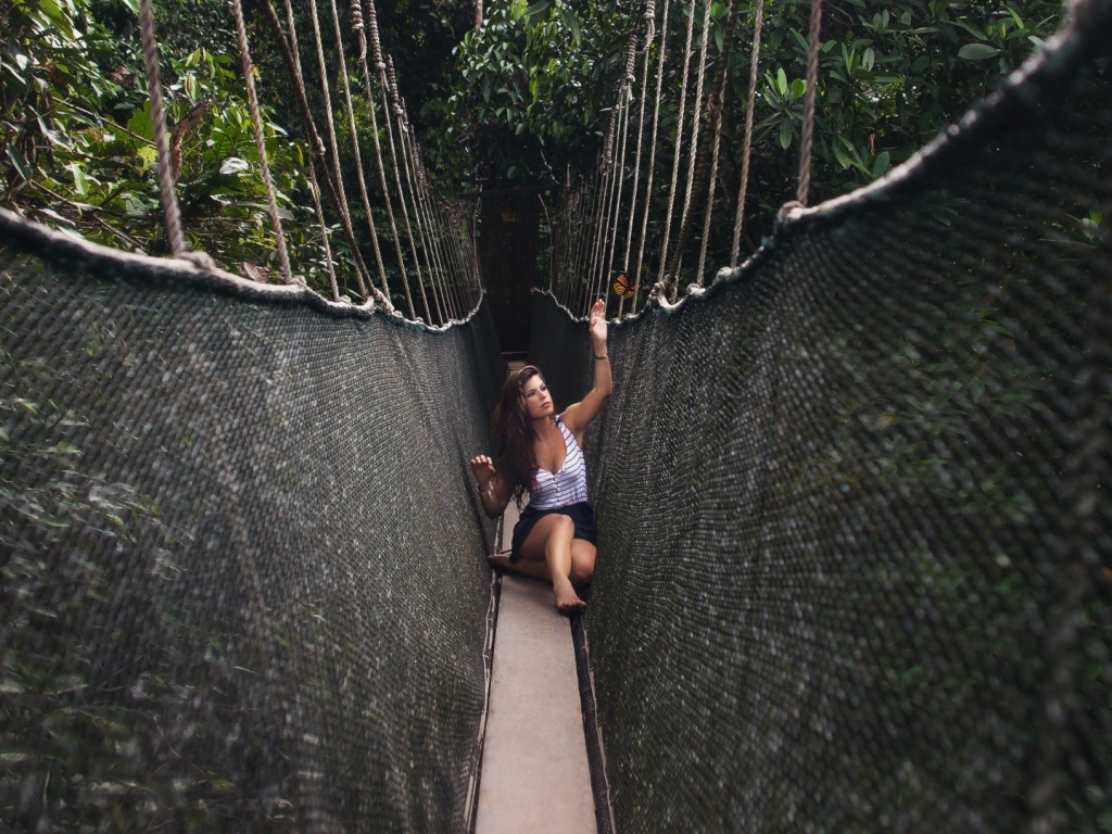 Девушка сидит на подвесном мосту