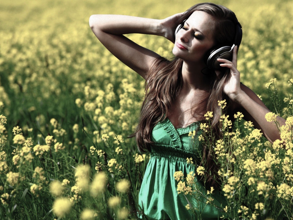 Девушка стоит среди цветов в наушниках