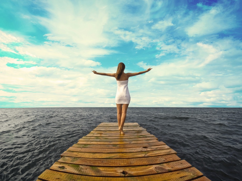 Девушка стоит раскинув руки на краю причала