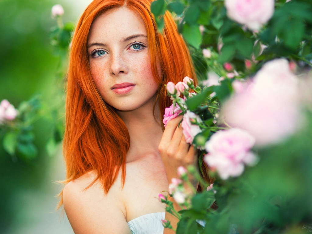 Рыжая девушка прячется за цветущими ветками