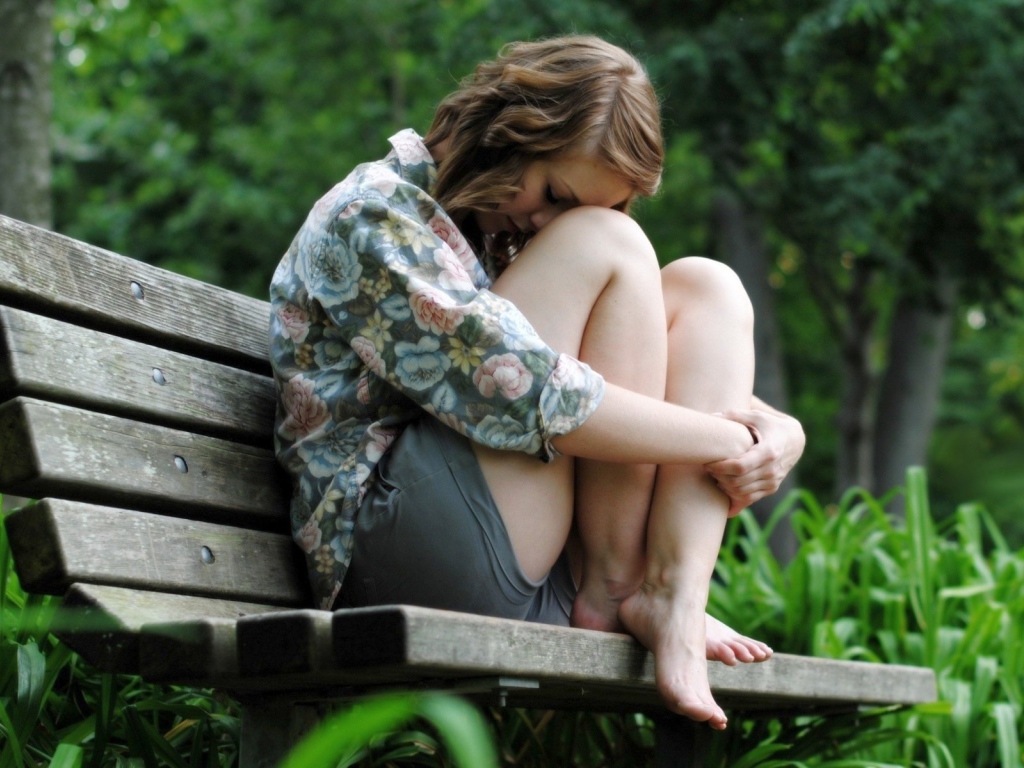 Девушка грустит сидя на скамье