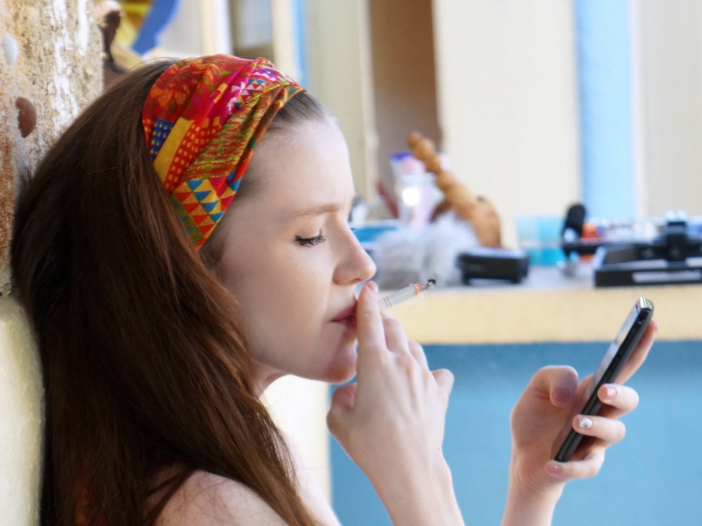 Девушка курит и смотрит на экран телефона