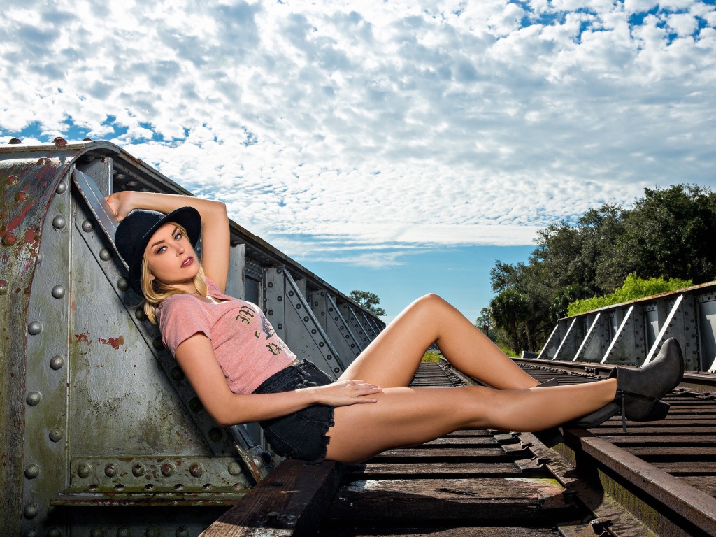 Блондинка в шляпе позирует на железной дороге