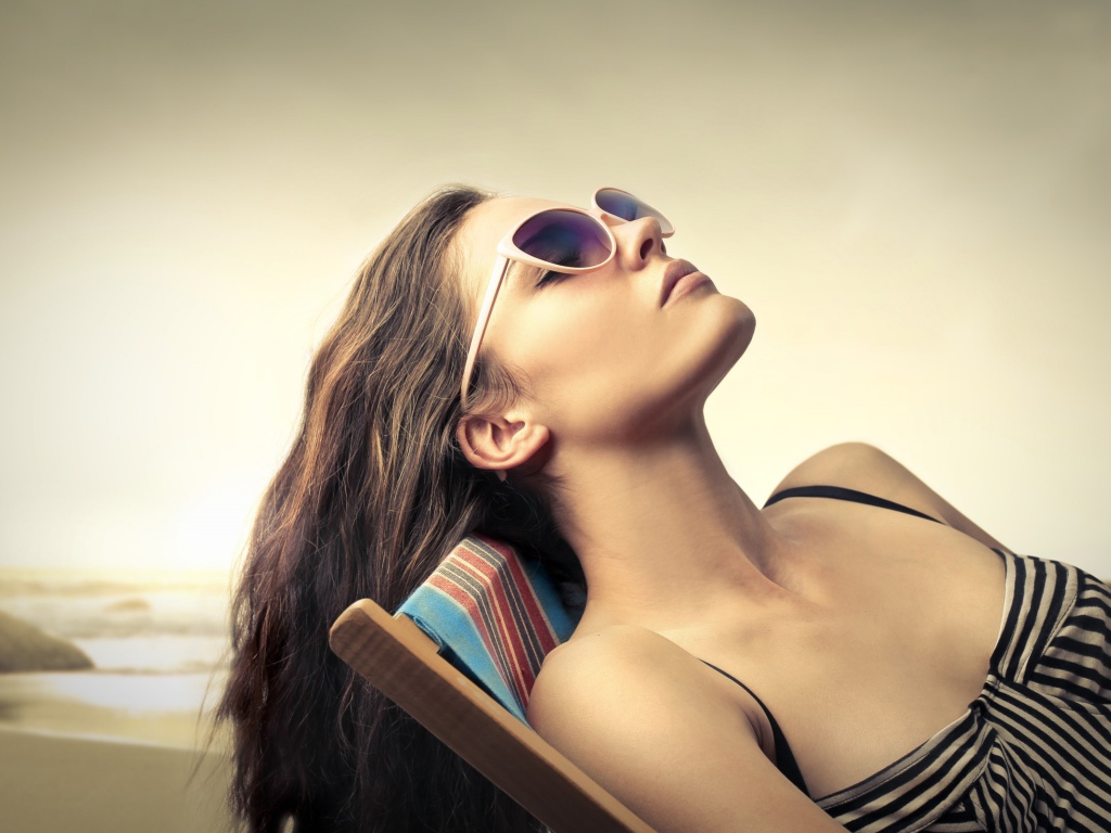 Девушка в очках загорает в шезлонге