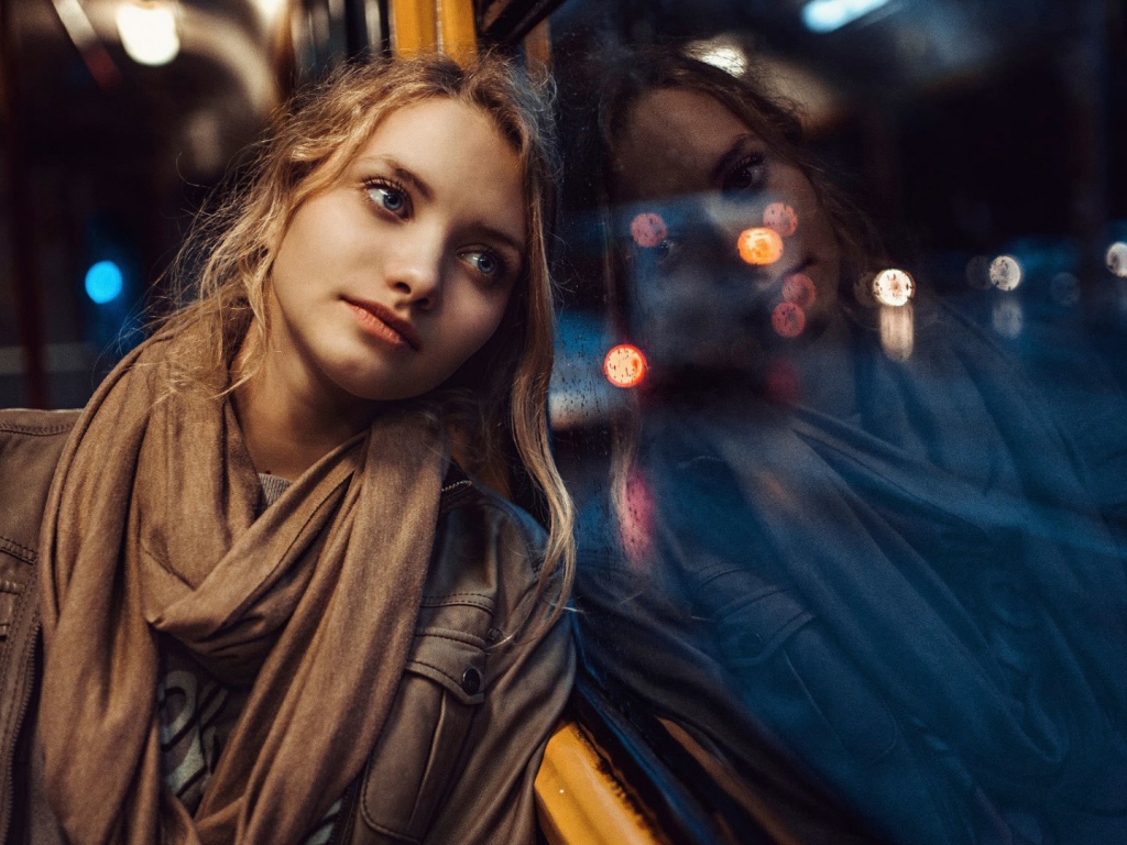 Девушка прислонилась к окну вечернего автобуса