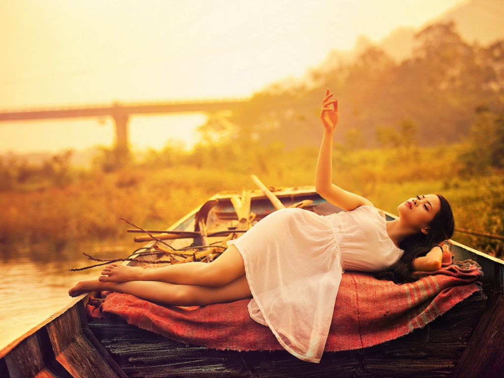 Азиатская модель в белом платье лежит в лодке