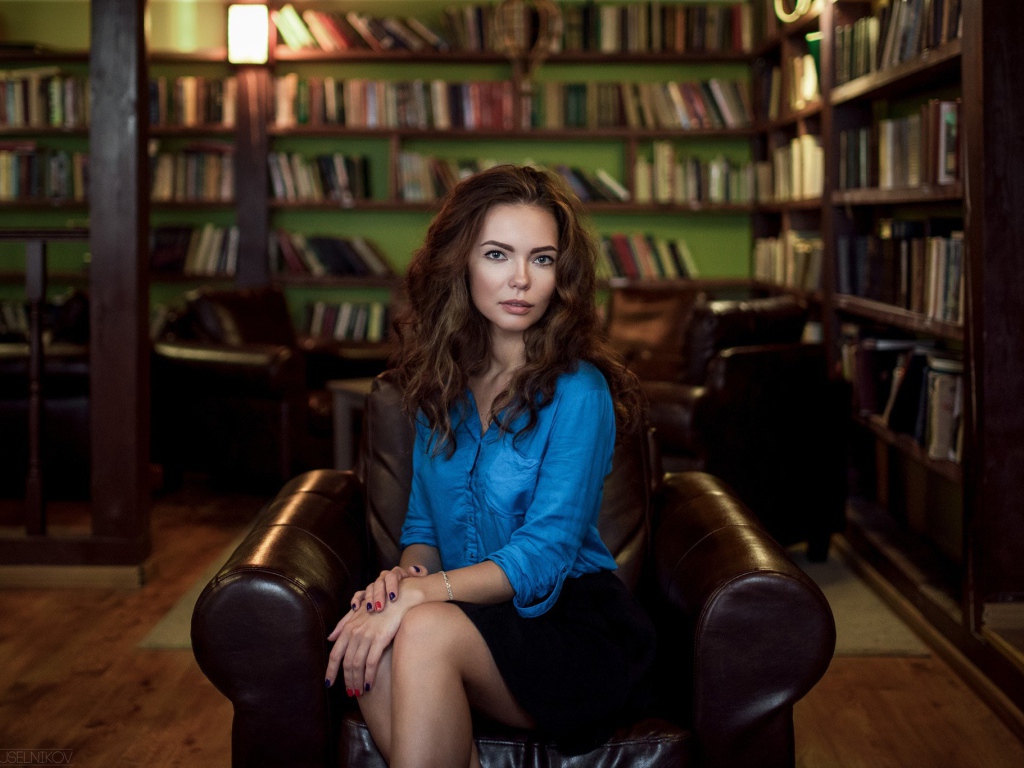 Модель в голубой блузке сидит на кожаном кресле