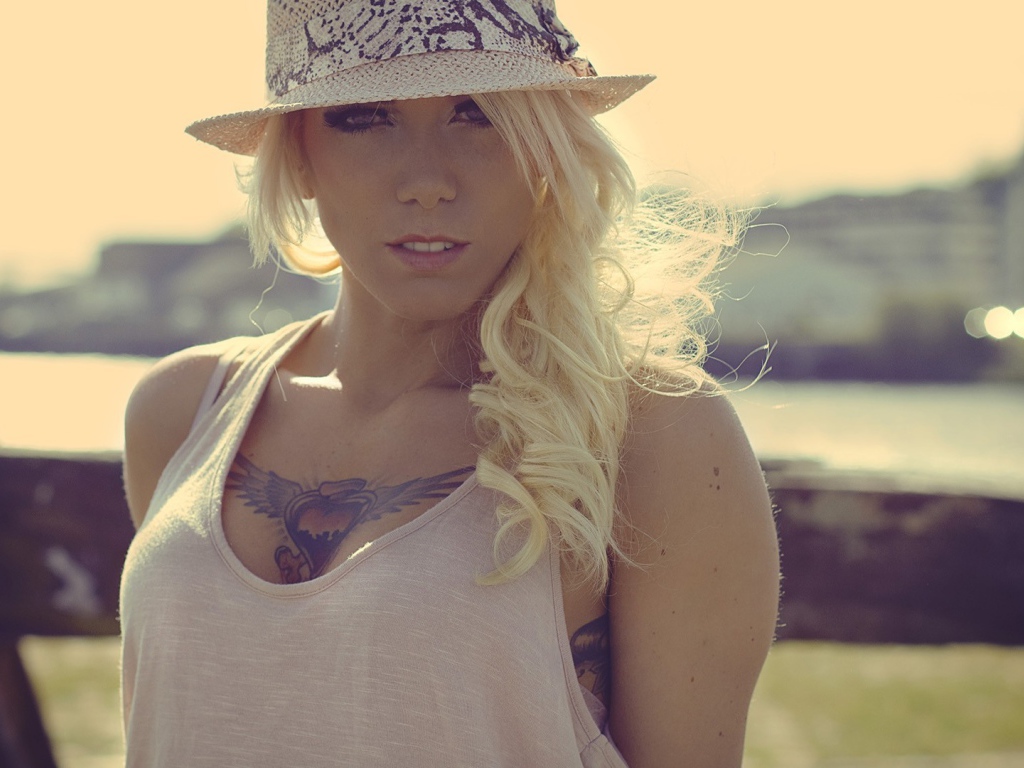 Блондинка в белой шляпе с тату на груди