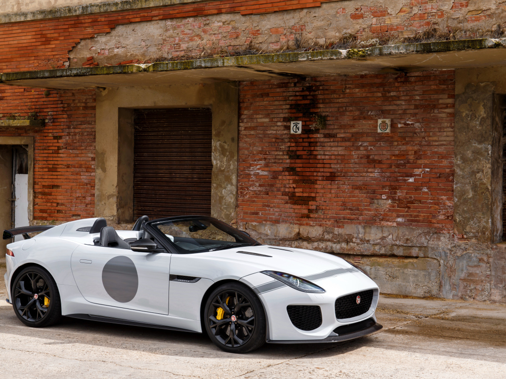 Белый автомобиль Jaguar F-Type у красной кирпичной стены