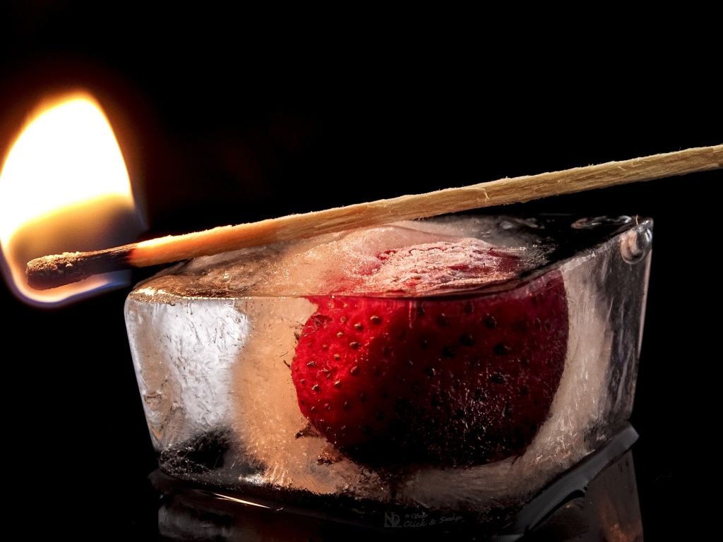 Зажженная спичка на кусочке льда с клубникой 