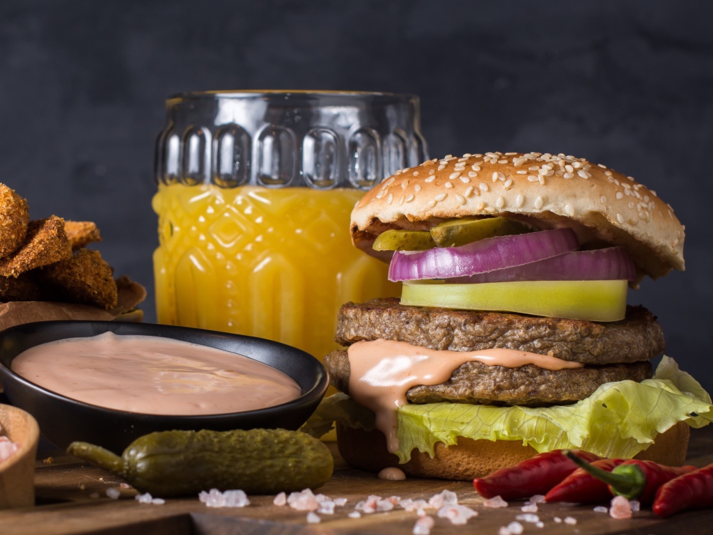 Аппетитный гамбургер на столе с соусом, овощами и соком