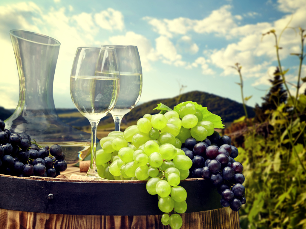 Гроздья синего и белого винограда с фужерами на деревянной бочке