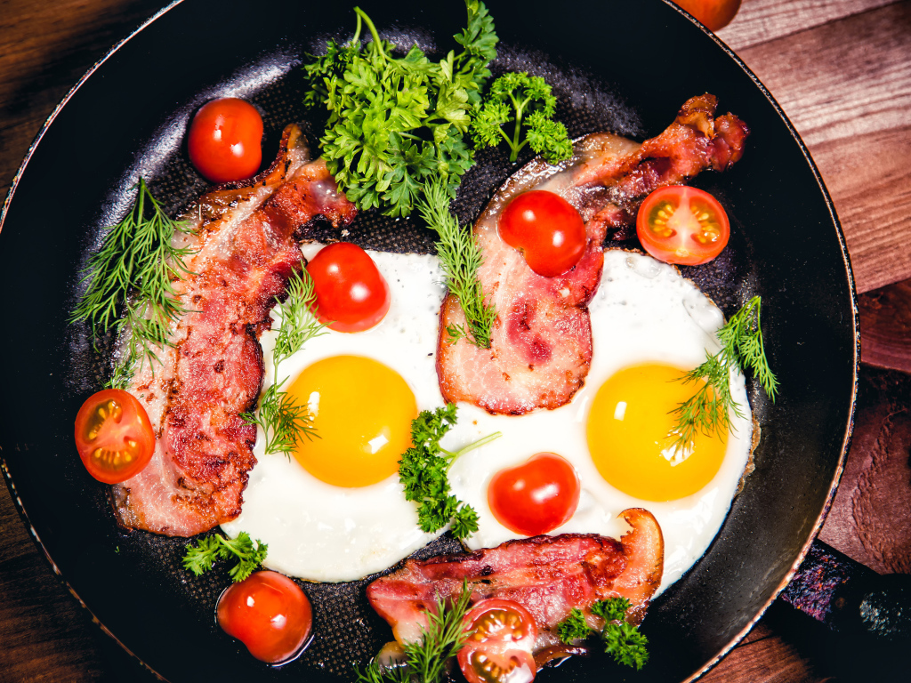Яичница с беконом, помидорами и зеленью в сковороде на завтрак