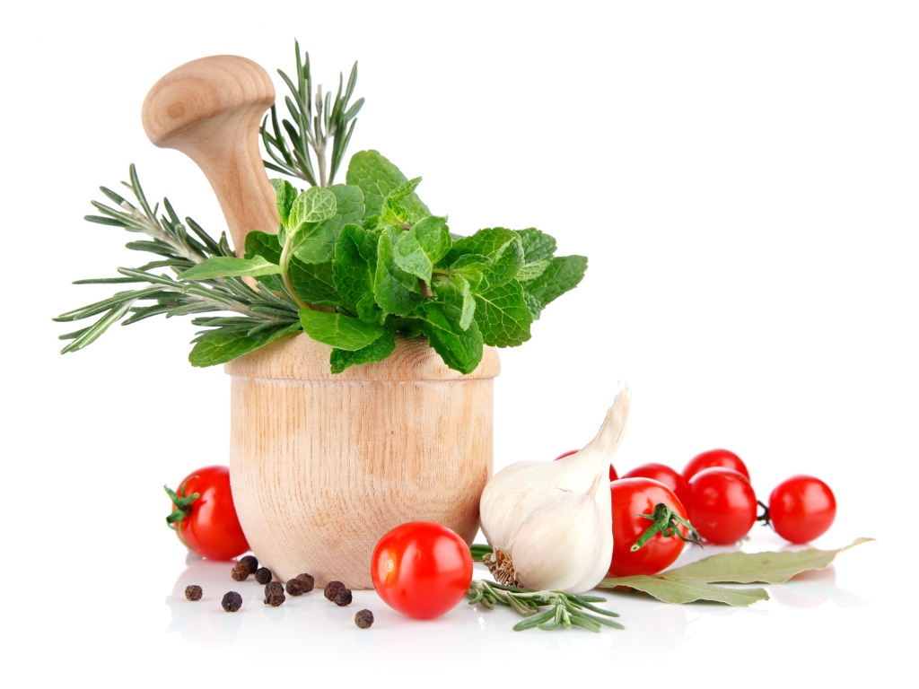 Деревянная ступа и пестик со специями и зеленью на столе с чесноком и помидорами