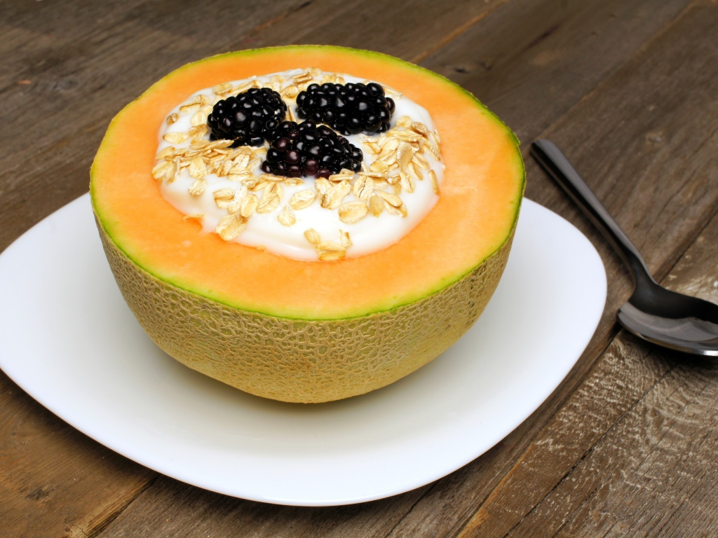 Йогурт с ежевикой и овсянкой в тарелке из свежей дыни на завтрак