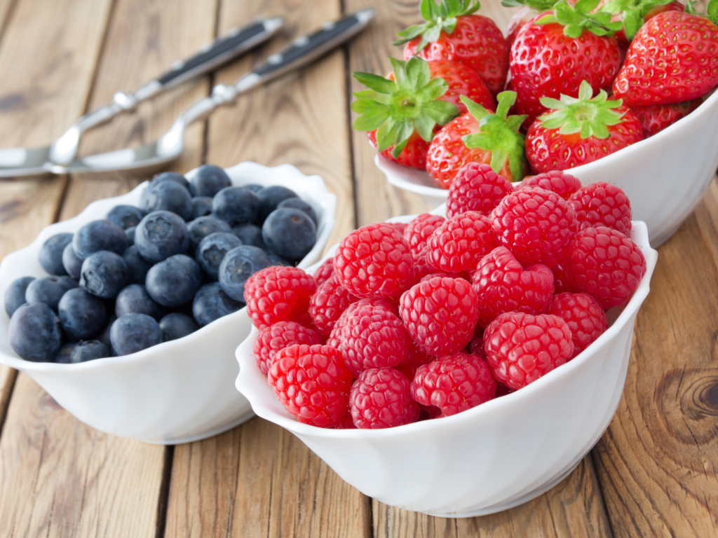 Свежие ягоды малины, клубники и черники в белых тарелках на столе