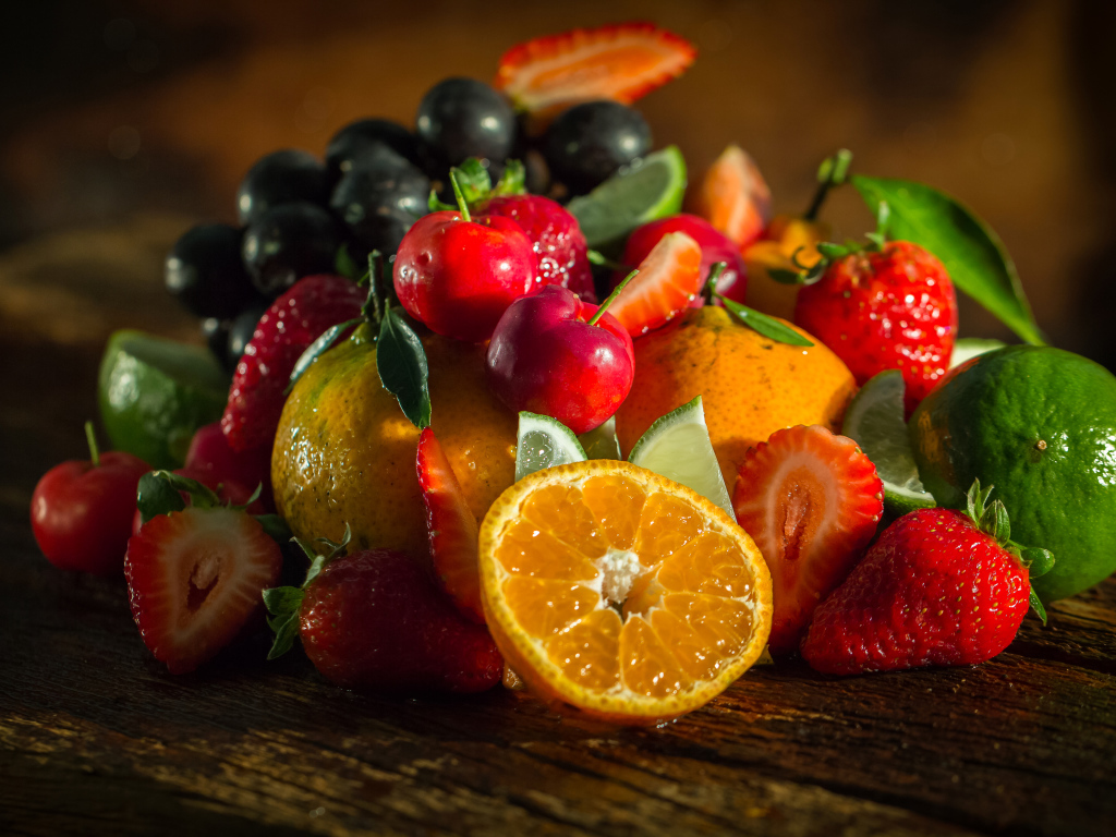 Свежие кусочки апельсина, лимона и ягоды вишни и клубники на столе