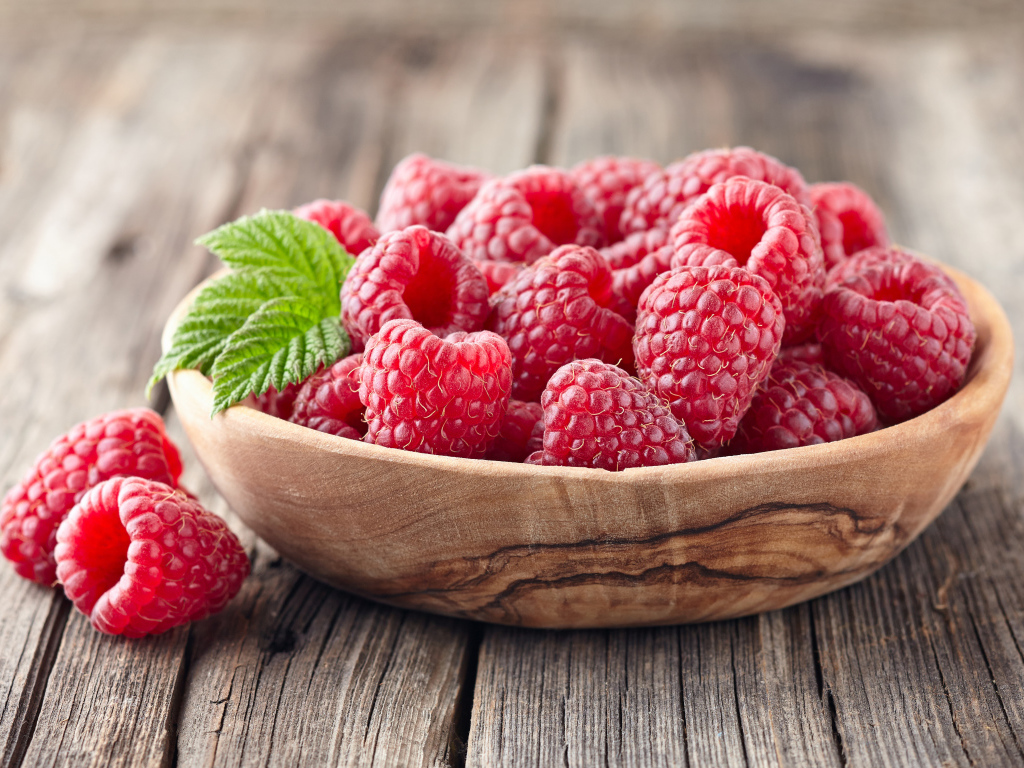 Крупные спелые ягоды малины в деревянной миске на столе