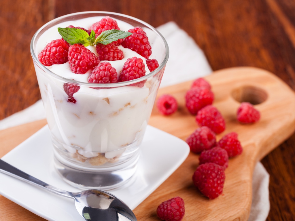 Десерт с йогуртом и свежей малиной в стеклянном стакане на столе