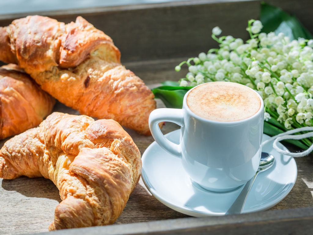 Свежие круассаны с чашкой кофе и букетом ландышей на столе