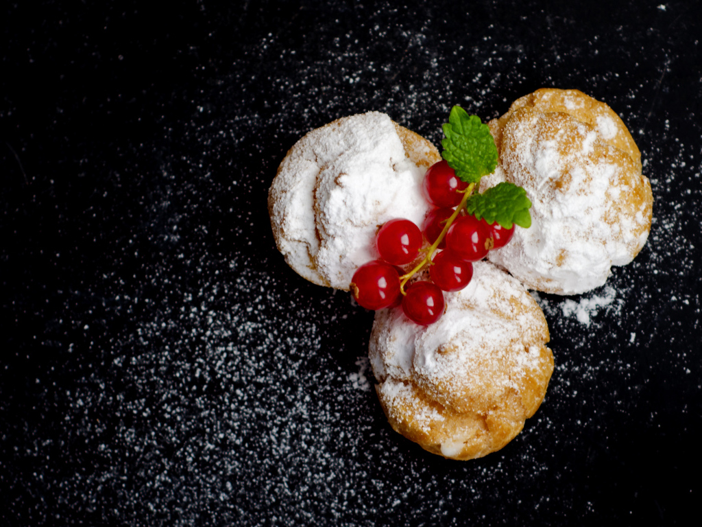 Три пирожных с сахарной пудрой и красной смородиной на черном фоне