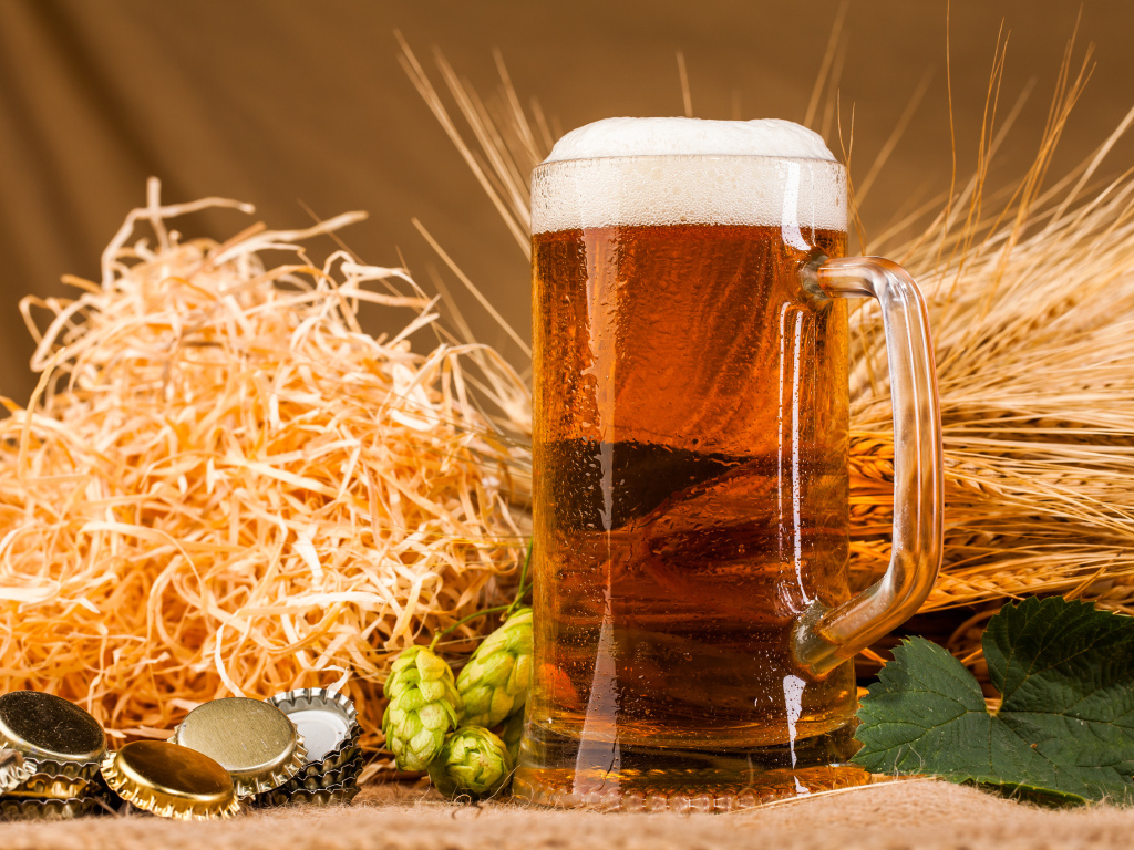 Бокал пива с пеной на столе с хмелем и соломой