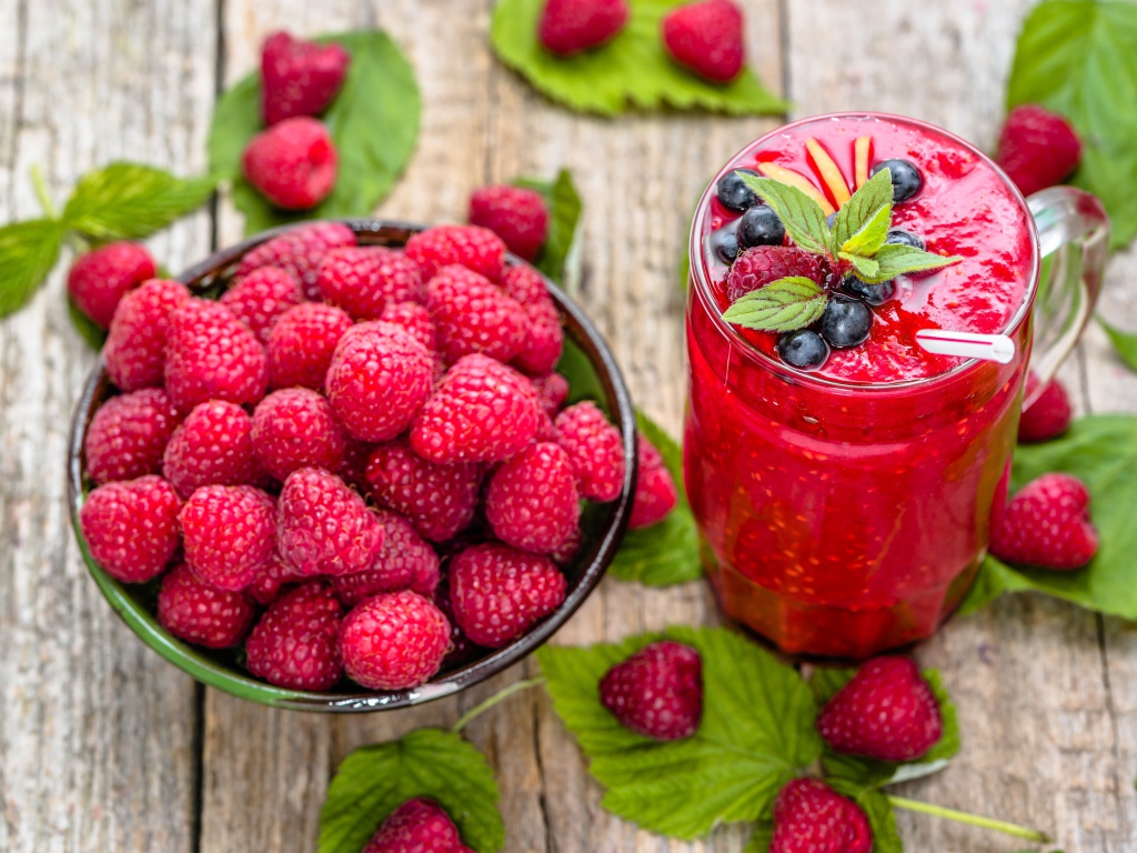 Стакан ягодного смузи на столе со свежими ягодами малины