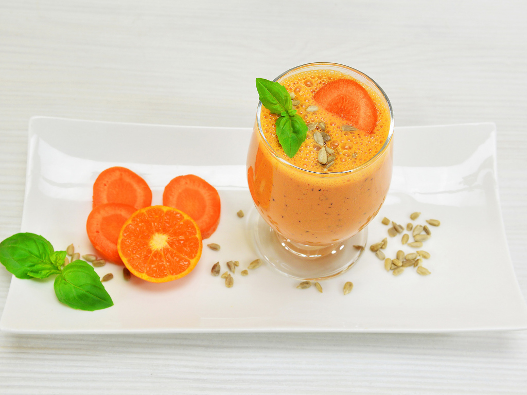 Бокал морковного коктейля с апельсином на белой тарелке