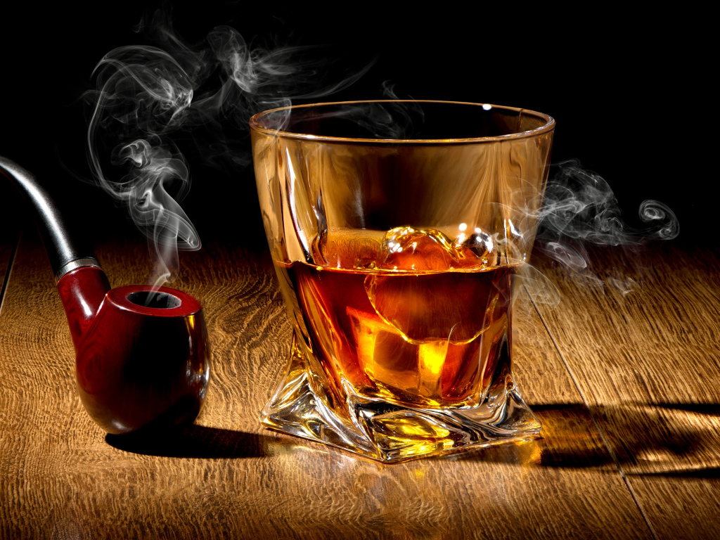 Стакан виски со льдом на столе с дымящейся трубкой