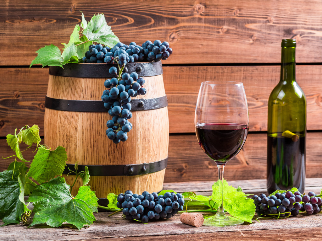 Бокал вина с бочкой и бутылкой на столе с гроздьями синего винограда с листьями