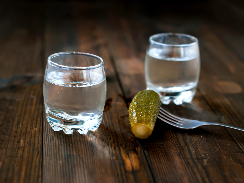 Две рюмки водки и соленый огурец на столе