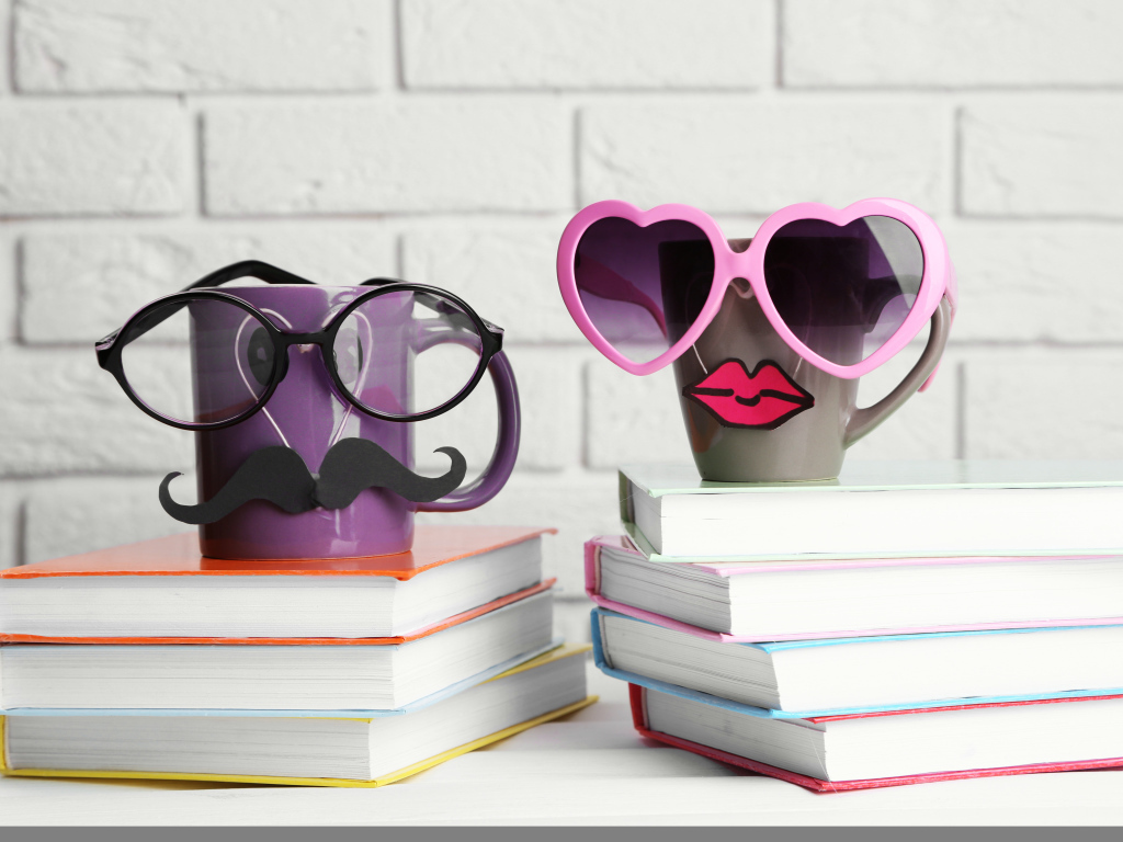 Две забавные чашки в очках стоят на книгах