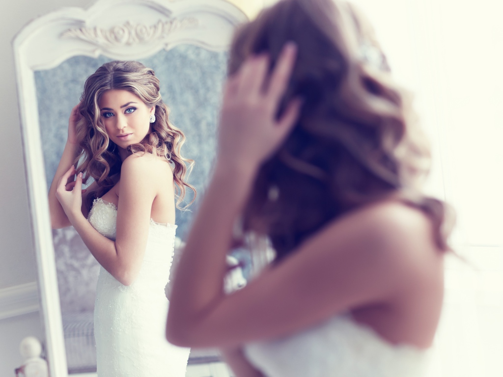 Красивая девушка в свадебном платье смотрит в зеркало 