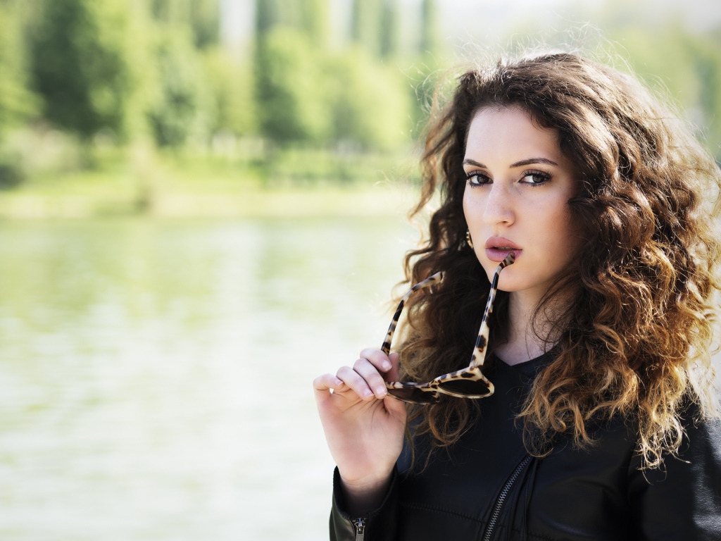 Красивая девушка с волнистыми волосами с очками в руках 