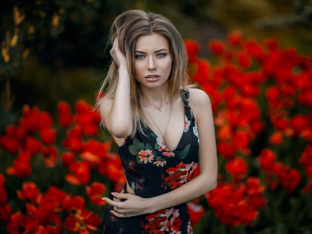 Красивая молодая девушка позирует на фоне красных тюльпанов